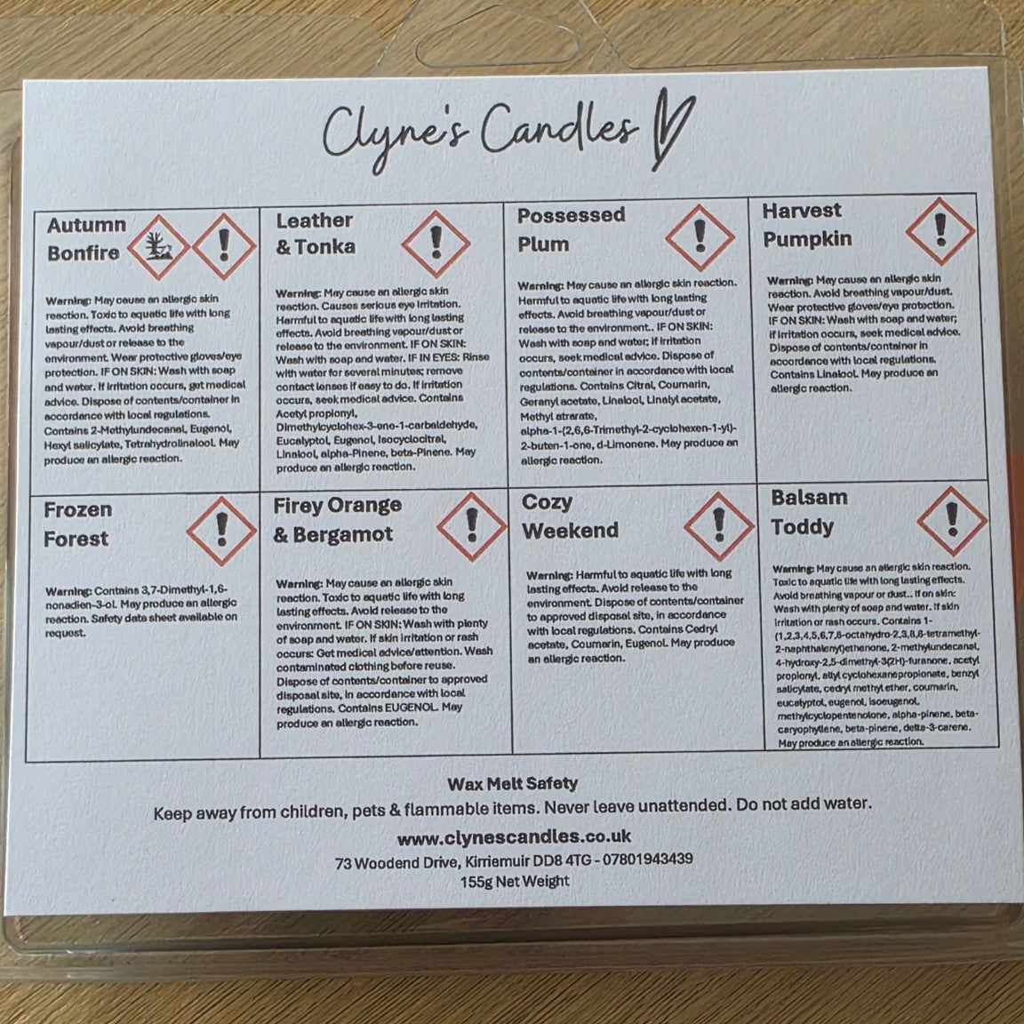 A printed product information sheet for Clyne's Candles, showing scent descriptions, hazard symbols, and wax melt safety information, placed on a light wood surface.