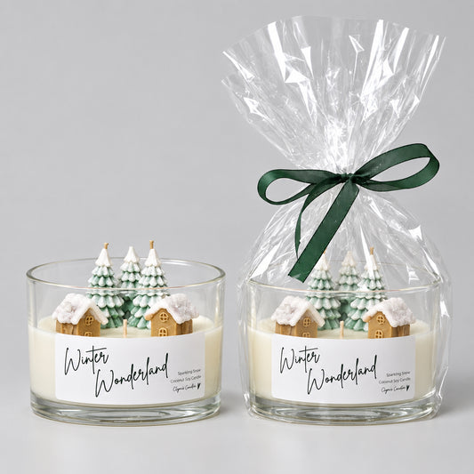 Two 'Winter Wonderland' scented candles displayed on a white shelf against a white wall. The left candle is in a clear glass jar with a white label and small decorative tree figures.