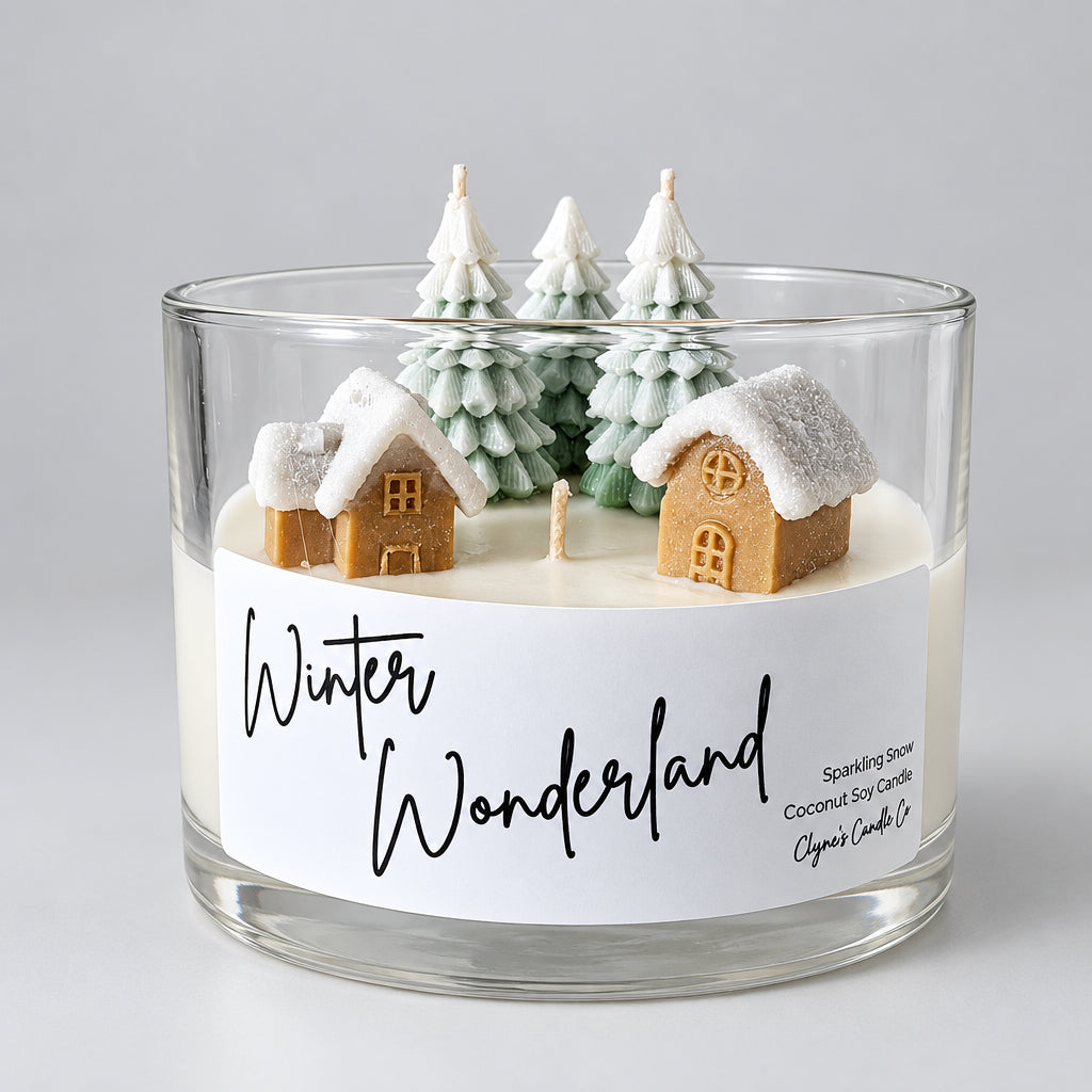 A clear glass jar candle labeled 'Winter Wonderland' with miniature snow-covered houses and evergreen trees on the wax surface, photographed against a plain light background.